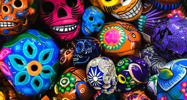 Stapel van fel beschilderde keramische schedels en ornamenten in levendige Día de Muertos kleuren.