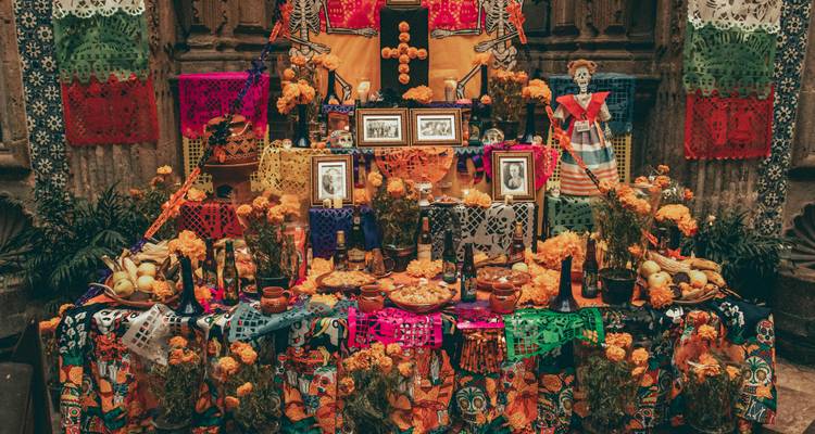 Weelderige Día de Muertos altaar met goudsbloemen, kaarsen, foto's, eten en kleurrijke papel picado versieringen.