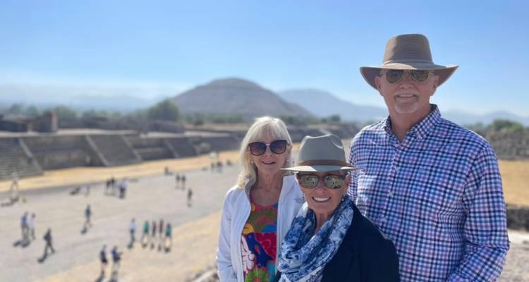 Drei Reisende lächeln in Teotihuacán mit der Sonnenpyramide im Hintergrund.