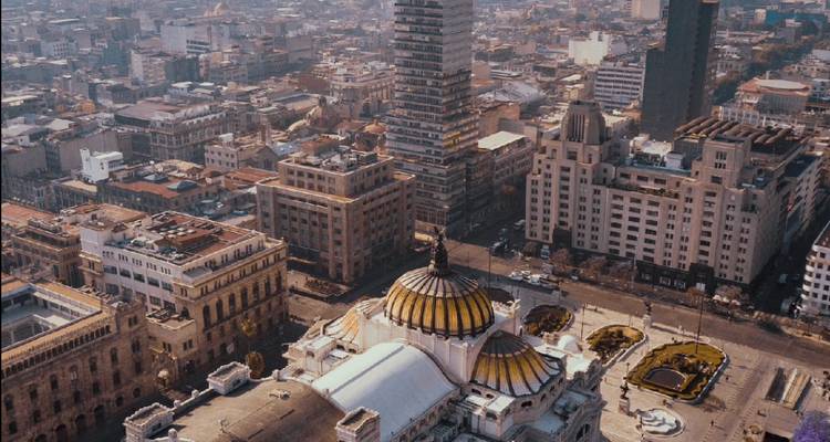 Luftaufnahme der Stadtlandschaft von Mexiko-Stadt mit dem goldkuppligen Palacio de Bellas Artes und den umliegenden Gebäuden der Innenstadt unter klarem Himmel.