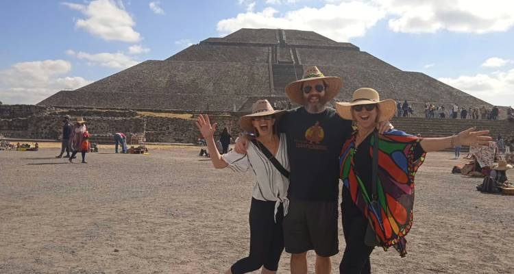 Drei fröhliche Reisende posieren vor der gewaltigen Sonnenpyramide in Teotihuacán an einem hellen Tag.