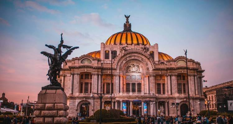 Der beleuchtete Palacio de Bellas Artes in der Dämmerung mit einem dramatischen rosa Himmel und Menschenmengen auf dem Platz.