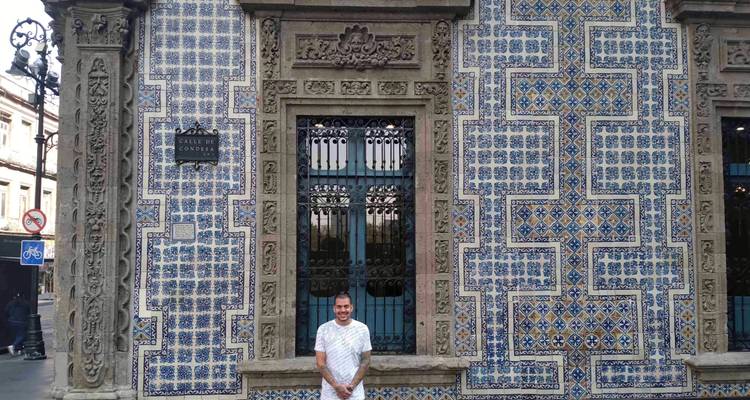 Ein Mann steht lächelnd vor der kunstvoll verzierten blau-weißen Kachelfassade der Casa de los Azulejos.