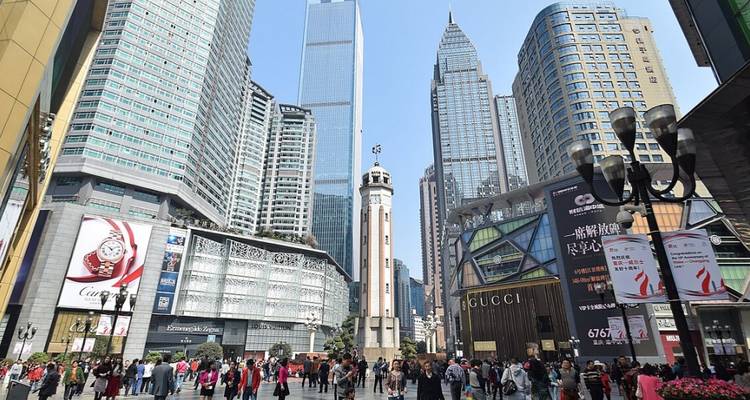 A busy pedestrian plaza surrounded by towering glass skyscrapers and luxury storefronts.