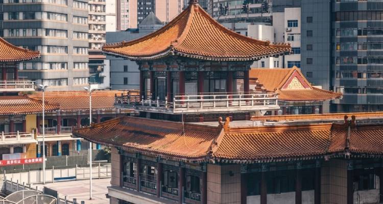 Traditional Chinese temple rooftop with ornate orange tiles set amid modern city buildings.
