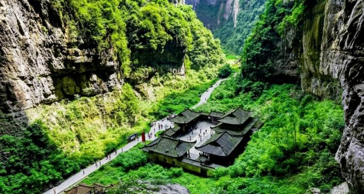 Lush green valley with traditional tiled buildings nestled between towering limestone cliffs.
