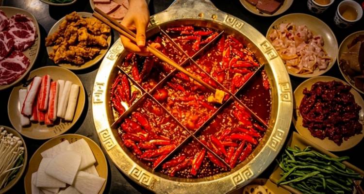 Top-down view of a bubbling nine-section hotpot surrounded by assorted meats, vegetables and spices.