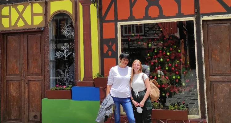 Dos mujeres sonríen afuera de un escaparate de entramado de madera pintado de colores brillantes y decorado para las fiestas.
