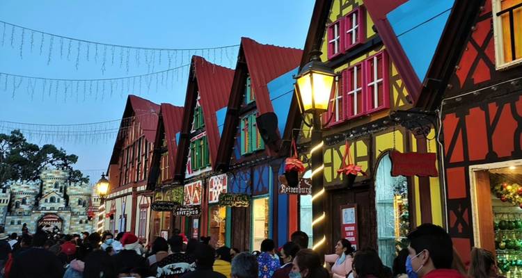 Las multitudes exploran una fila festiva de escaparates coloridos de estilo alpino al anochecer mientras las luces comienzan a brillar.
