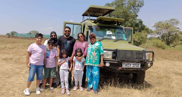 Family group posing in front of green safari truck on grassy plain.