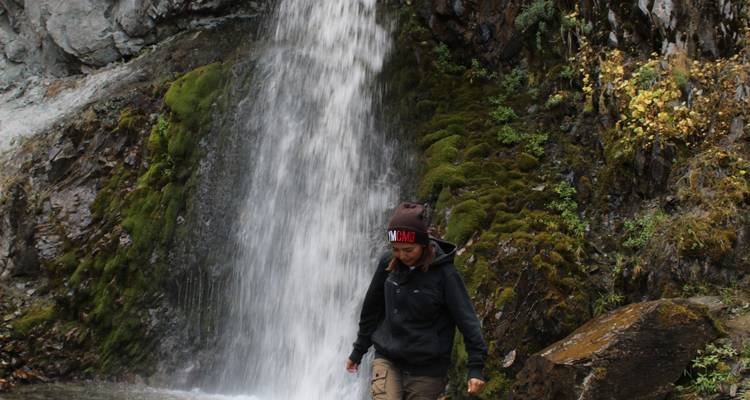 Wandelaar in buitenuitrusting die loopt naast een met mos bedekte waterval in een weelderige kloof.