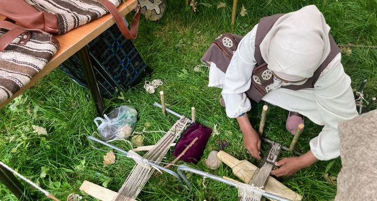 Lokale ambachtsvrouw die op een grondgetouw weeft te midden van groen gras op een culturele buitenmarkt.