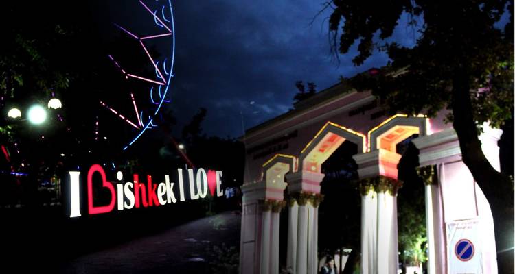 Nachtscène van een verlicht 'I Bishkek Love' bord met een reuzenrad op de achtergrond.