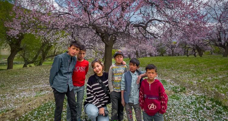 Toeristische en lokale kinderen die onder bloeiende kersenbomen staan met bloemblaadjes op het gras