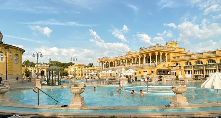 Piscinas termales al aire libre de los Baños Széchenyi en Budapest con edificios neoclásicos amarillos.