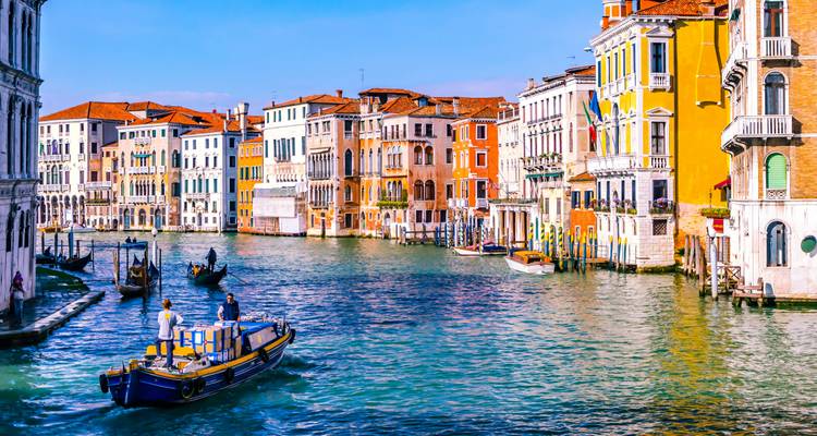 Edificios venecianos coloridos que bordean el Gran Canal con embarcaciones transportando mercancías.