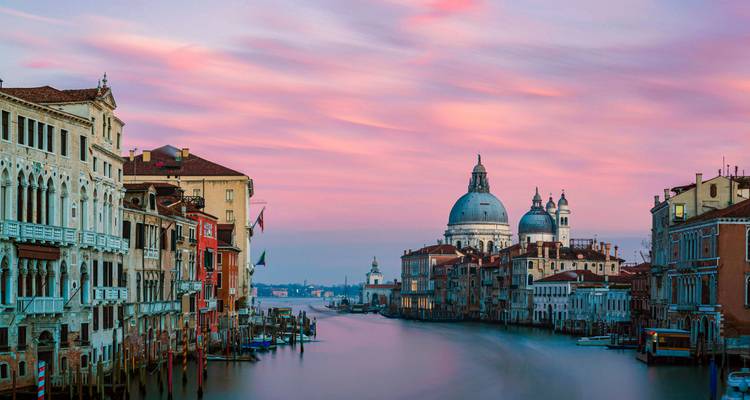 Vista del atardecer por el Gran Canal hacia Santa Maria della Salute con cielo rosa pastel sobre Venecia.