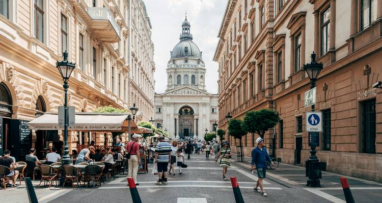 Calle peatonal en Budapest que lleva a la Basílica de San Esteban con terrazas de café al aire libre y compradores.