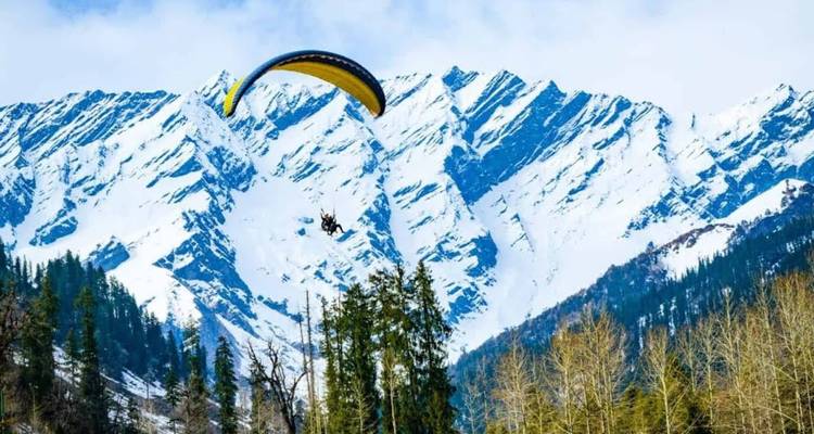 Paraglider, der vor dramatischen schneegestreiften Himalaya-Gipfeln mit immergrünen Bäumen darunter schwebt.