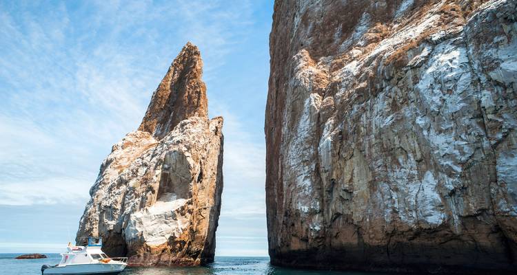 Dramatic volcanic rock formation known as Leon Dormido rises sharply from the sea beside a small tour boat.