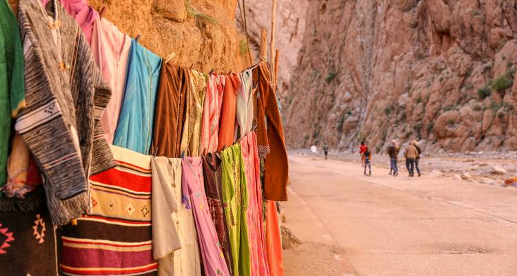 Los textiles coloridos cuelgan a lo largo de la pared del cañón en la Garganta de Todra mientras los caminantes pasan por el camino.