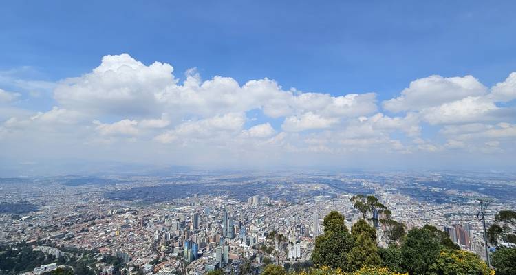Vue panoramique en haute altitude surplombant l'étendue urbaine de Bogotá vers les montagnes lointaines sous un ciel nuageux parsemé.