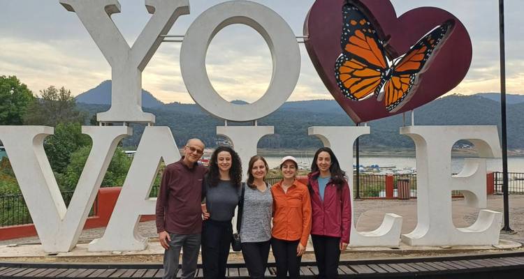 Familia posando frente al gran letrero de mariposa YO VALLE con vista a un lago y colinas