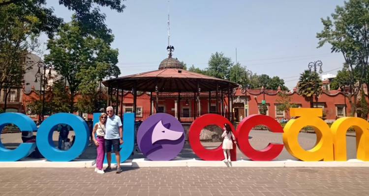 Turistas posando junto a las coloridas letras de COYOACÁN en una plaza con un kiosco