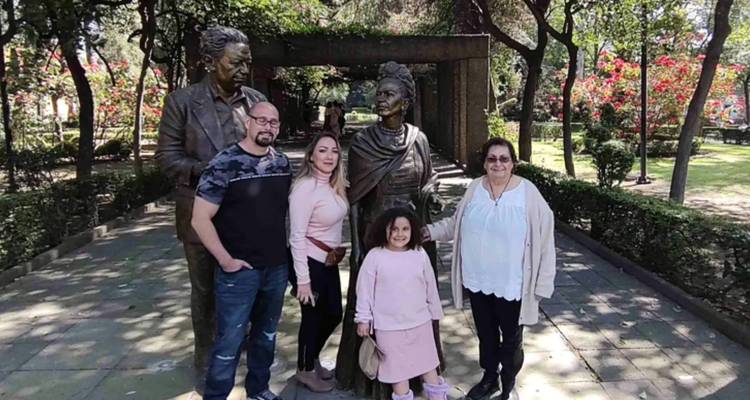 Familia posando con estatuas de bronce de famosos artistas mexicanos en un parque frondoso