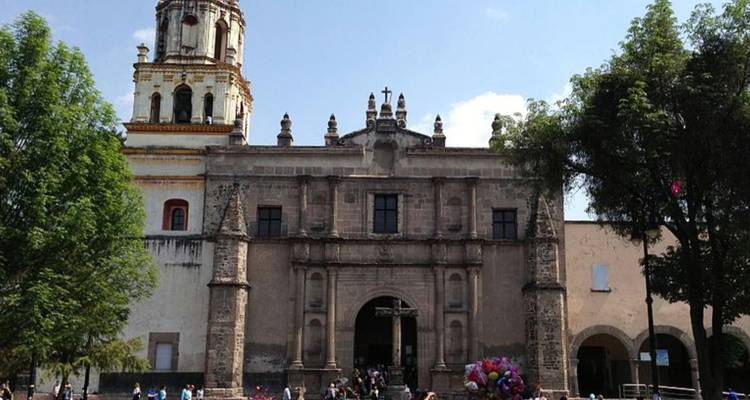 Fachada de iglesia colonial de piedra con visitantes y vendedores de globos al frente