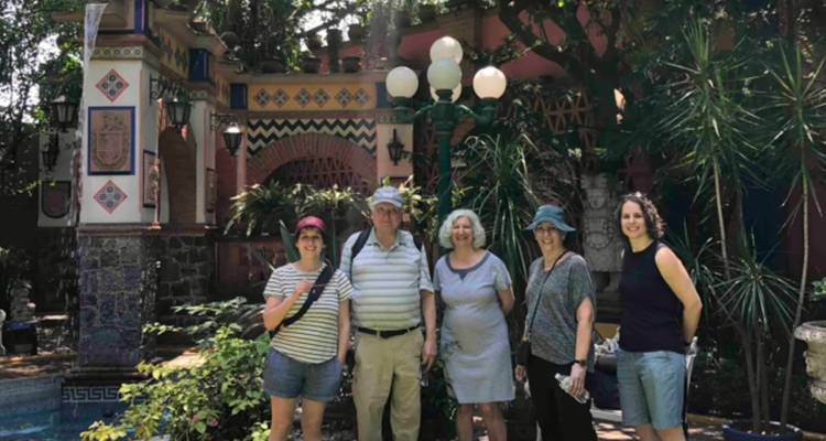 Pequeño grupo de turistas posa en un patio exuberante con azulejos ornamentados y faroles