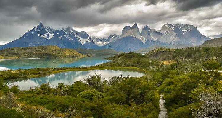 Las nubes melancólicas cuelgan sobre los picos dentados de la Patagonia reflejados en lagunas tranquilas y bosques verde denso.