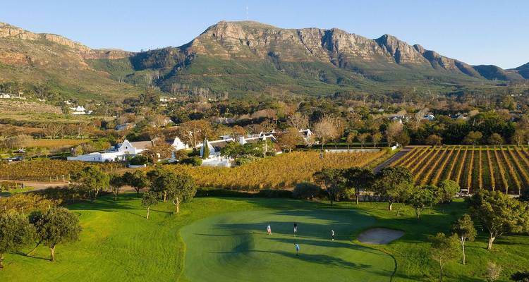Grüner Golfplatz und Weinberge vor schroffen Bergen im warmen Nachmittagslicht