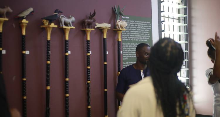 Besucher hören einem Führer in einem Museum zu, das traditionelle ghanaische Stäbe ausstellt.