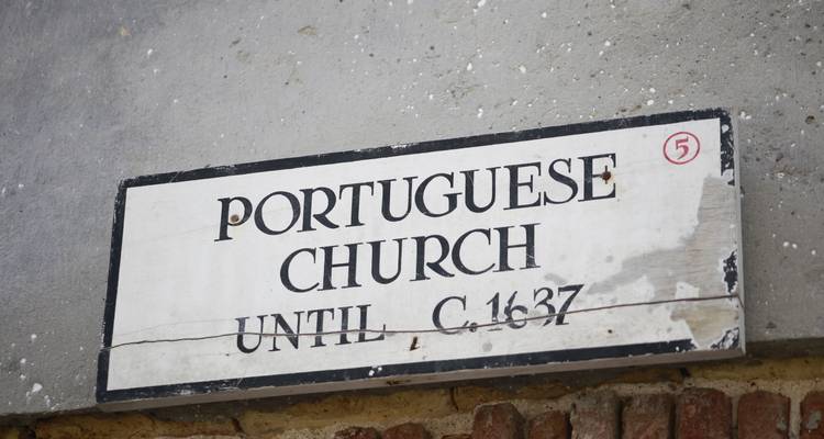 Verwittertes Schild mit der Aufschrift „Portugiesische Kirche bis ca. 1637" an einer alten Festungsmauer.