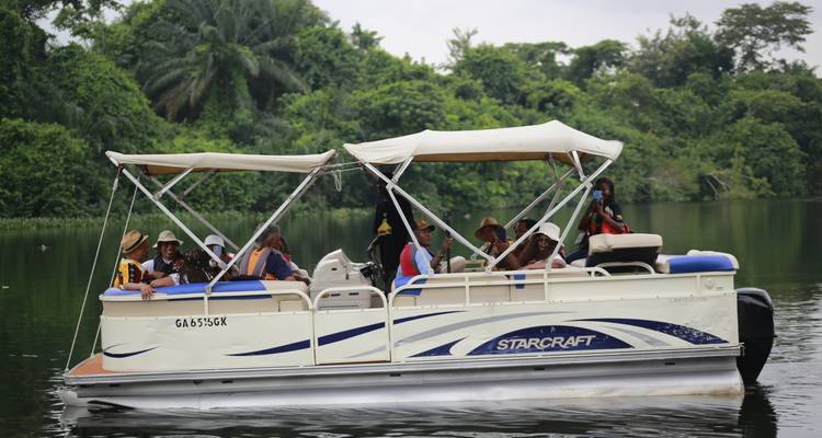Ein offenes Pontonboot mit Touristen gleitet entlang eines üppigen, von Bäumen gesäumten Flusses.