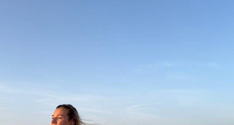 Junge Frau genießt das Licht der goldenen Stunde, während sie auf einer weiten Wüstendüne unter einem klaren blauen Himmel steht.