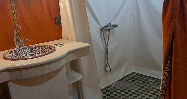 Einfaches Zeltbadezimmer mit marokkanischem Waschbecken, offener Dusche und gemustertem Fliesenboden.