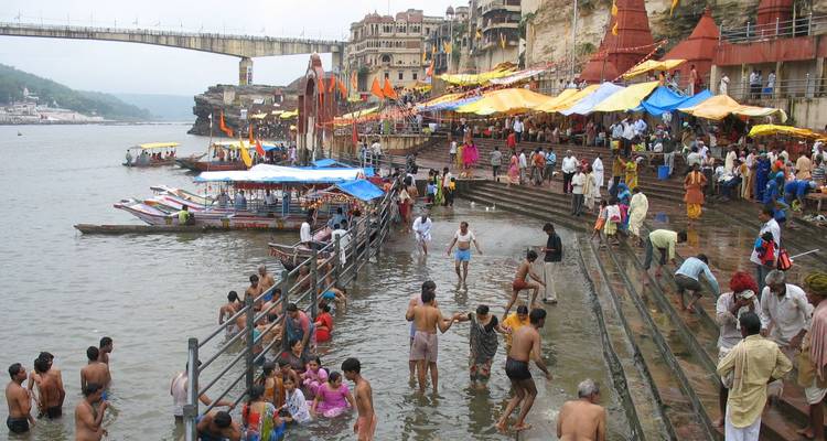 Les pèlerins et les habitants se rassemblent sur les ghats à gradins pour les bains rituels au bord d'une large rivière.