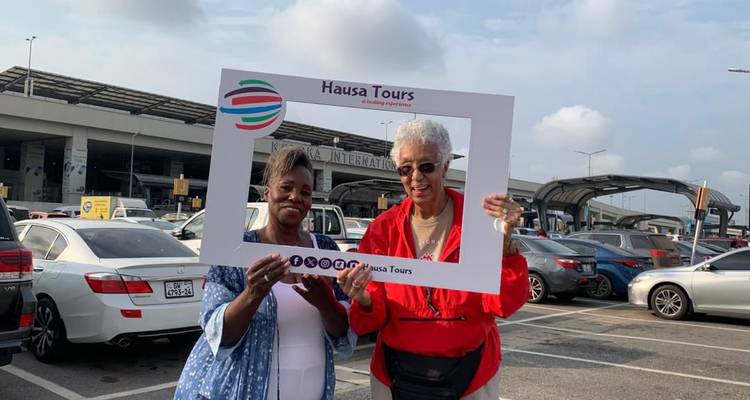Deux femmes tiennent un cadre de visite de marque à l'extérieur d'une zone d'arrivées d'un aéroport international.