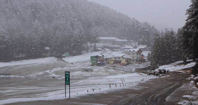 Schneefall hüllt ein Seeufer-Dorf und die umliegenden Kiefernwälder unter einem grauen Himmel ein.