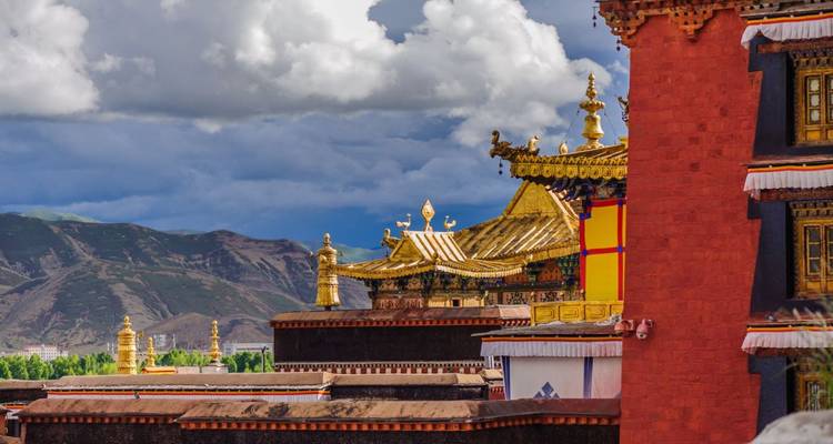 Goldene Dachdetails eines tibetischen buddhistischen Tempels heben sich gegen dramatische Bergwolken ab.