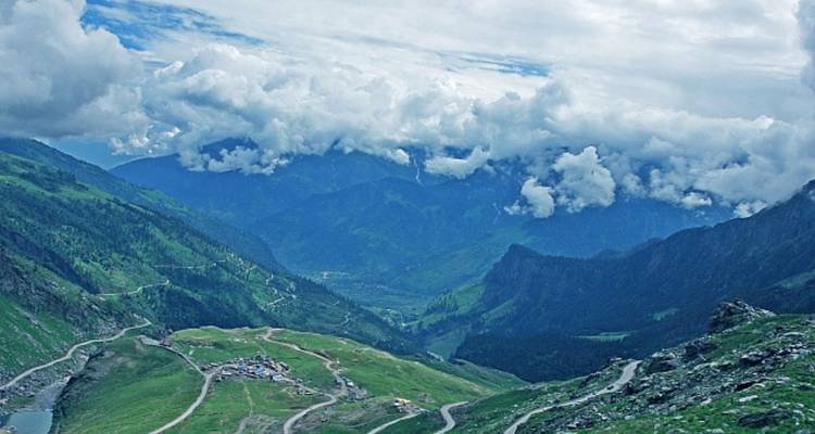 Eine sich windende Bergstraße schlängelt sich durch das nebelige, grüne Kullu-Tal zu fernen Gipfeln hin.