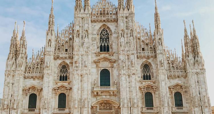 Fachada frontal del Duomo gótico de Milán con agujas intrincadas y detalles de mármol contra un cielo despejado.