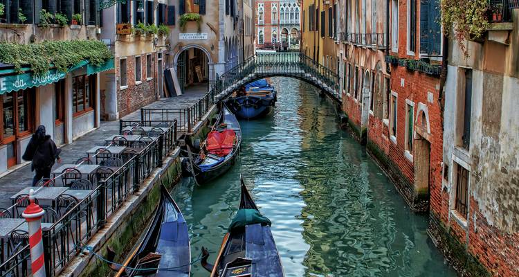 Pintoresco canal estrecho en Venecia con góndolas amarradas bajo un pequeño puente arqueado.