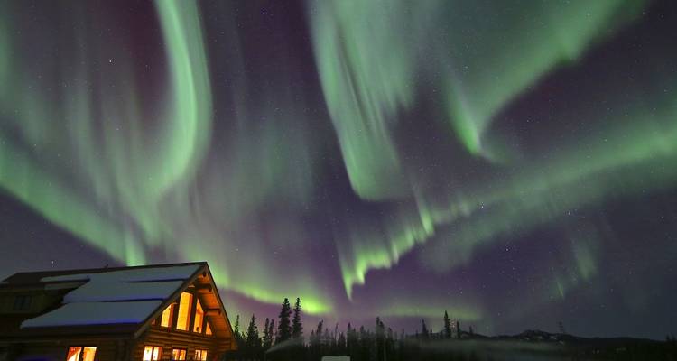 Brillantes cortinas de aurora boreal danzando sobre una cabaña cubierta de nieve.