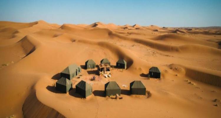 Vista aérea de un campamento circular de tiendas rodeado por dunas doradas ondulantes en el Sahara