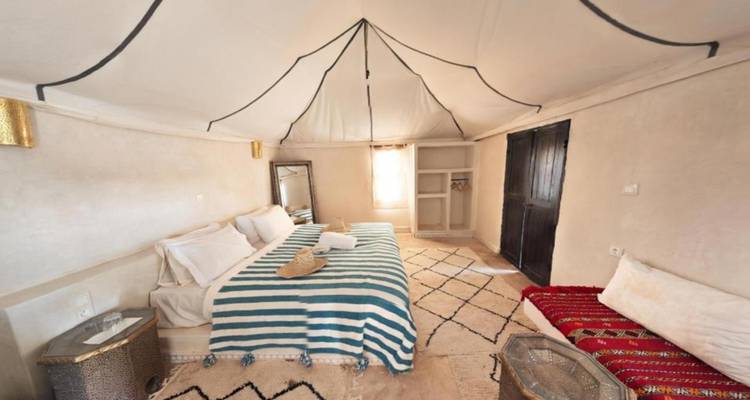 Dormitorio ligero de campamento desértico con colcha a rayas, techo de lona blanca y alfombras tradicionales