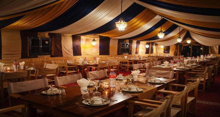 Gran carpa beréber de comedor con techo ricamente drapeado, faroles y mesas largas preparadas para la cena