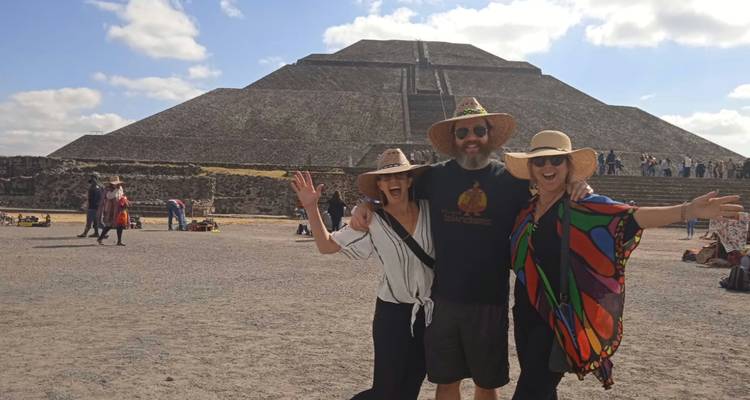 Drei glückliche Reisende posieren mit erhobenen Armen vor der Sonnenpyramide in Teotihuacán